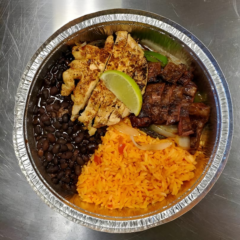 Compadres' Mexican dish with grilled chicken, steak, black beans, rice, and a lime wedge in a foil container.